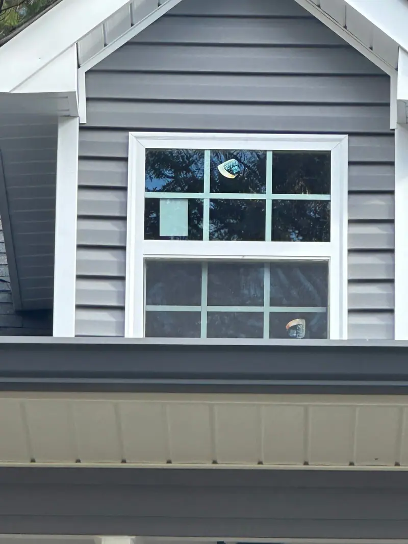 New double-hung window in a gable of gray lap siding above a dark gutter, a Mosqueda Construction window job