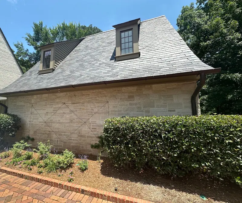 Stone home with a steep slate-style roof and dark half-round gutters, a Mosqueda Construction gutter job near Birmingham, AL