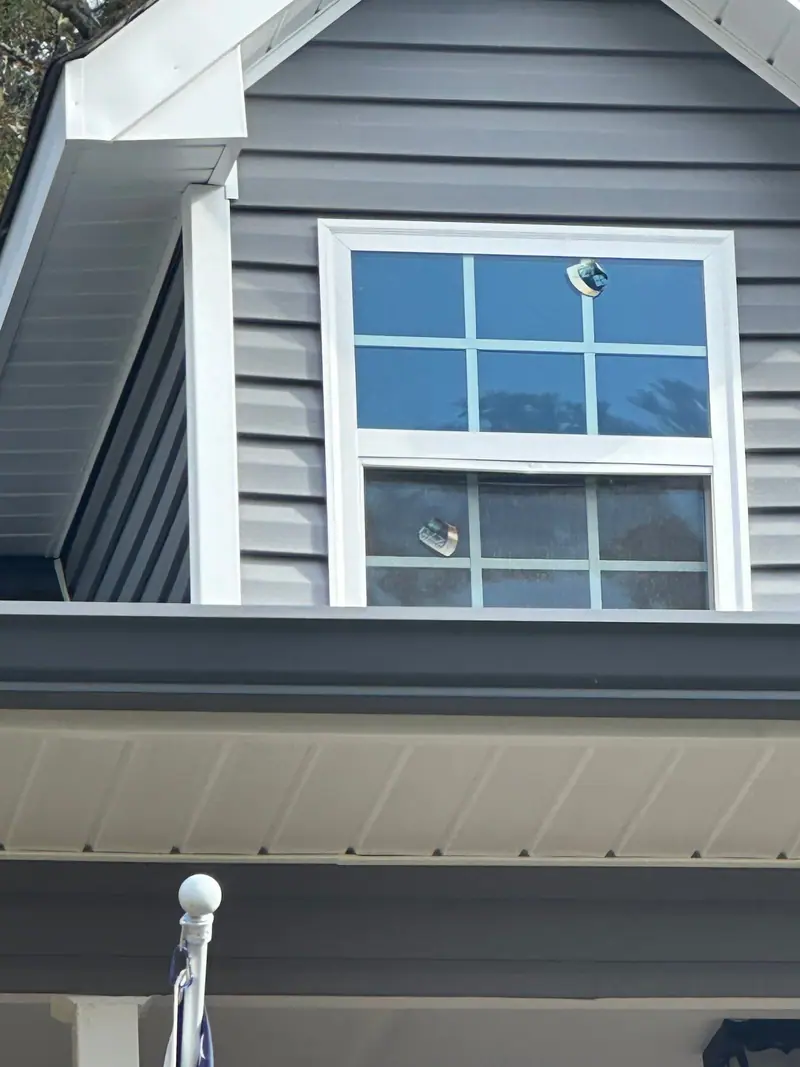 Newly installed double-hung window with factory stickers still on the glass, set in gray lap siding